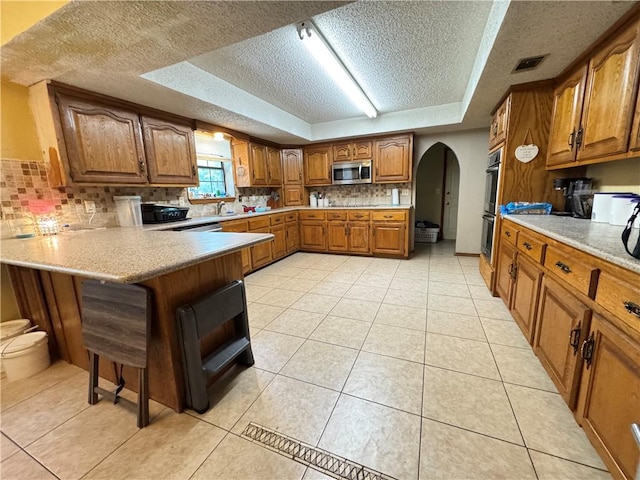 60 N Redwood Cir, Sallisaw, OK 74955 - kitchen featuring a peninsula, brown cabinets, a tray ceiling, arched walkways, and appliances with stainless steel finishes