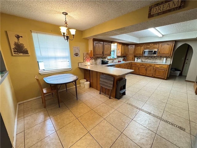 60 N Redwood Cir, Sallisaw, OK 74955 - kitchen featuring brown cabinetry, a peninsula, stainless steel microwave, arched walkways, and a wealth of natural light