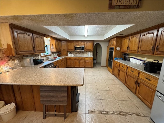 60 N Redwood Cir, Sallisaw, OK 74955 - kitchen featuring brown cabinetry, appliances with stainless steel finishes, arched walkways, light countertops, and a peninsula