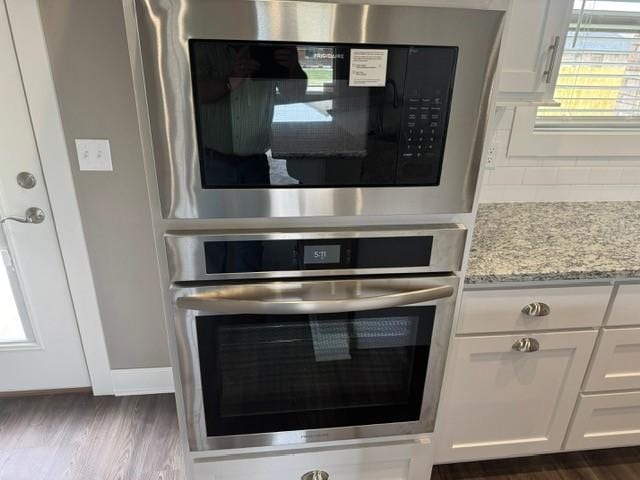interior details with backsplash, appliances with stainless steel finishes, light stone countertops, dark wood-style floors, and white cabinetry