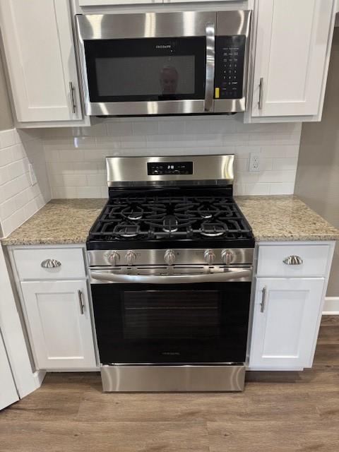 681 Baggett St, Prairie Grove, AR 72753 - kitchen with decorative backsplash, wood finished floors, light stone countertops, white cabinetry, and stainless steel appliances