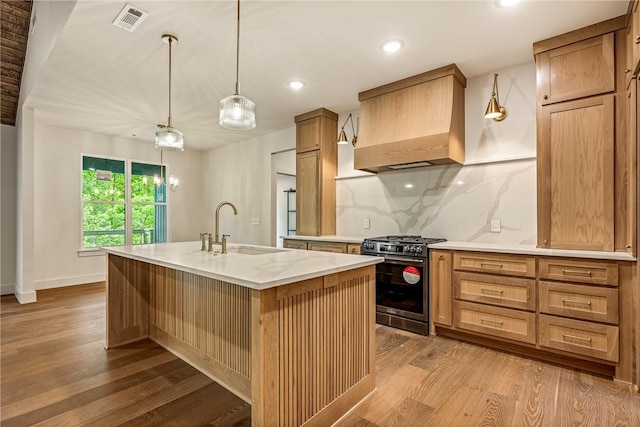 kitchen with a sink, light wood-style floors, gas range, visible vents, and custom exhaust hood