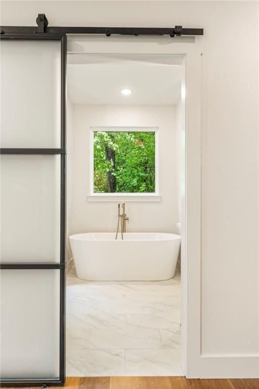 bathroom with marble finish floor and a freestanding tub