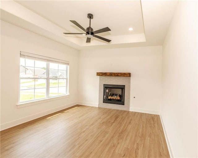 unfurnished living room with a raised ceiling, a fireplace, light wood-style floors, a ceiling fan, and baseboards