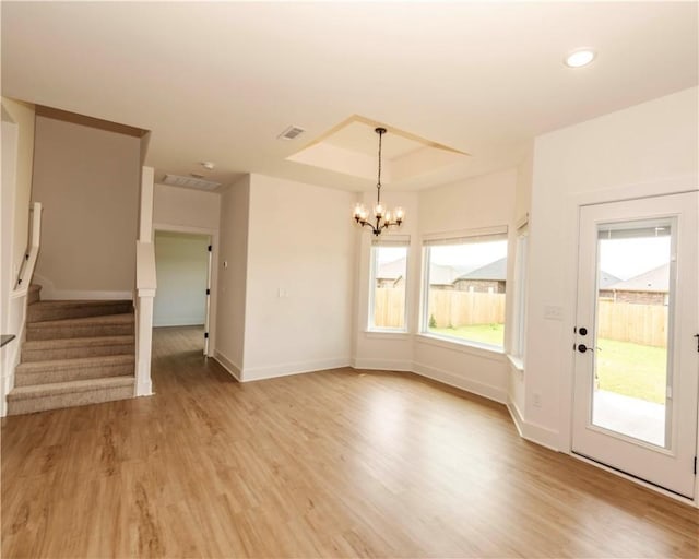 unfurnished living room with light wood-type flooring, stairway, baseboards, a raised ceiling, and a chandelier