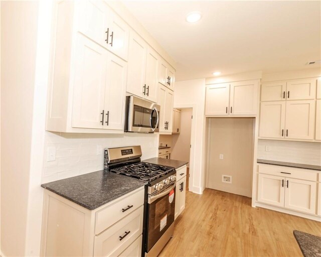 kitchen featuring backsplash, white cabinetry, appliances with stainless steel finishes, and light wood-style floors