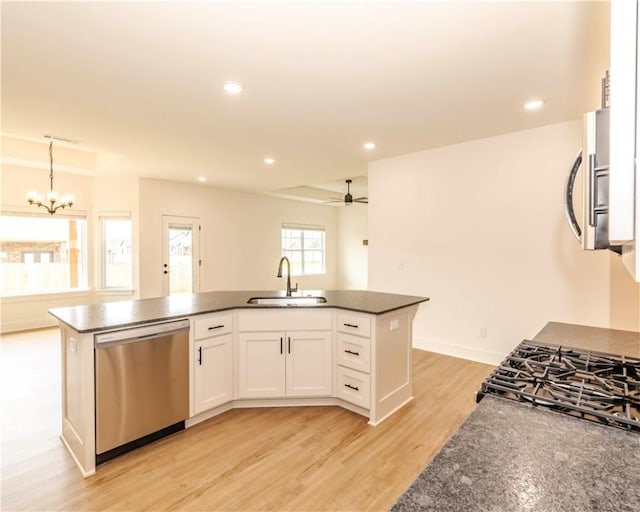 kitchen with appliances with stainless steel finishes, a sink, white cabinets, ceiling fan with notable chandelier, and an island with sink
