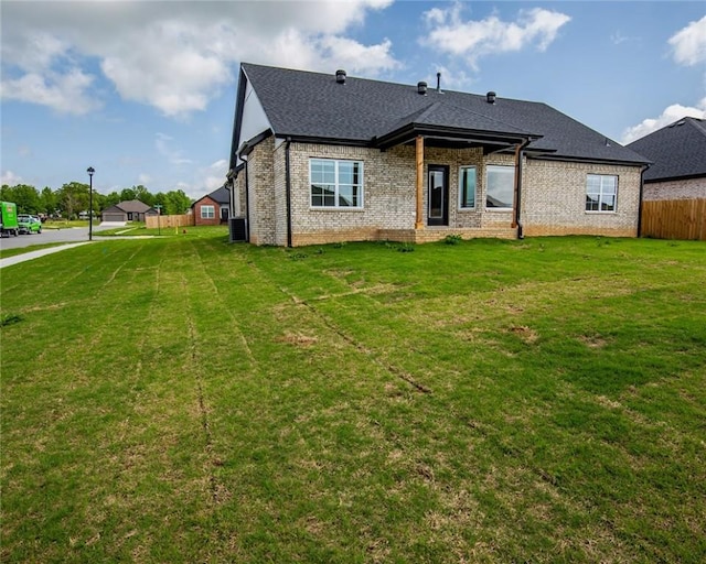 rear view of property featuring a lawn, brick siding, fence, and a shingled roof