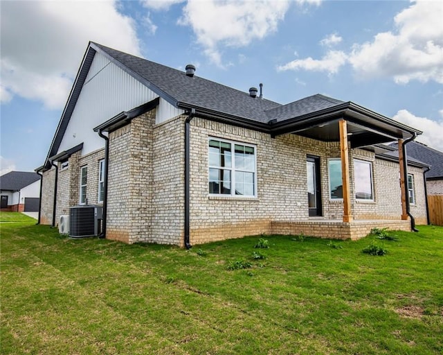 back of property with a lawn, central AC unit, brick siding, and a shingled roof