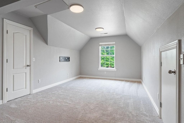 additional living space with a textured ceiling, baseboards, lofted ceiling, and carpet