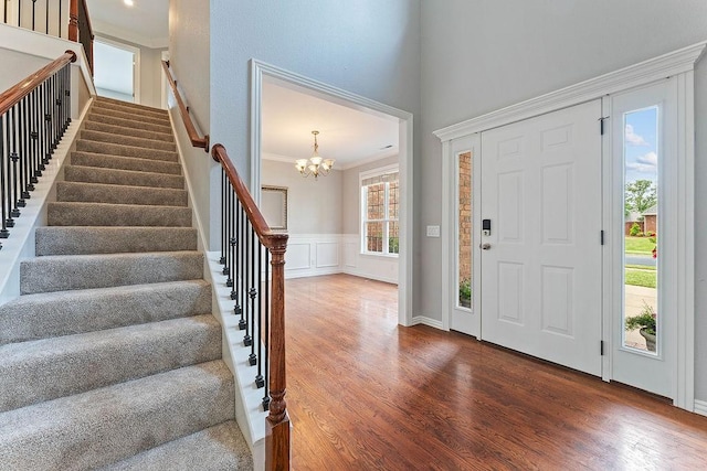 entryway with crown molding, wainscoting, wood finished floors, stairway, and a chandelier