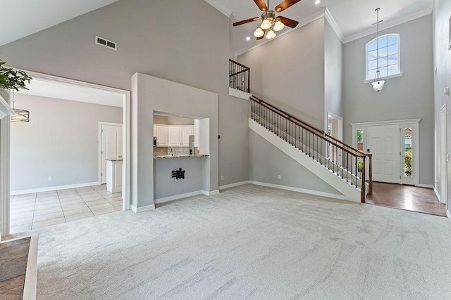 unfurnished living room featuring visible vents, crown molding, a towering ceiling, light carpet, and ceiling fan