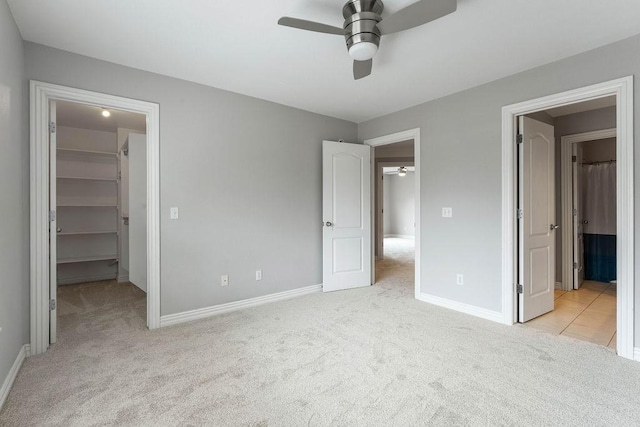 unfurnished bedroom featuring a ceiling fan, baseboards, a spacious closet, and light carpet