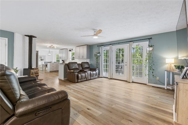 living room featuring ceiling fan, visible vents, a wood stove, light wood-type flooring, and baseboards