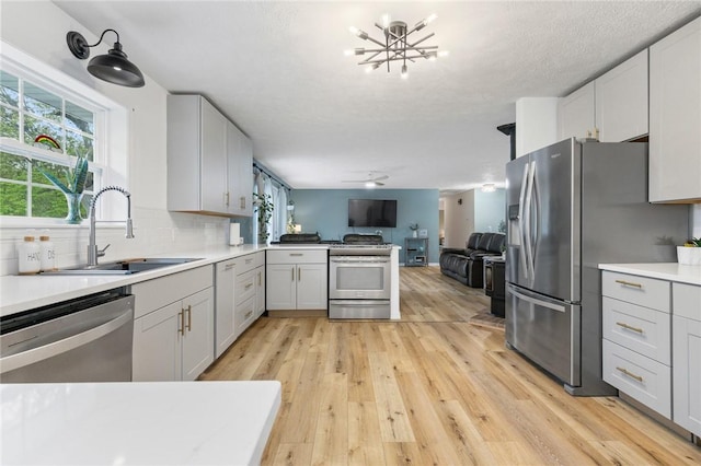 kitchen with open floor plan, light countertops, a sink, light wood-style flooring, and appliances with stainless steel finishes