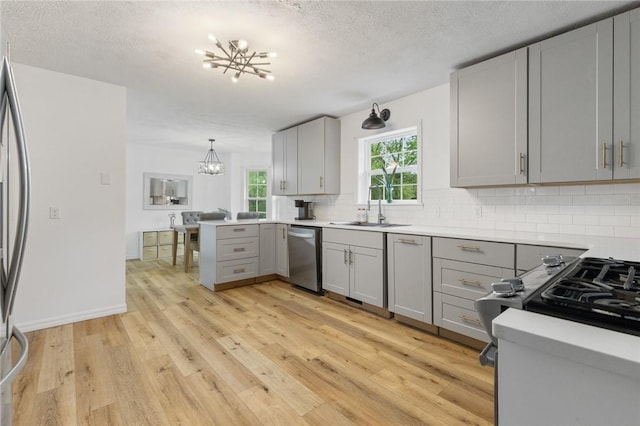 kitchen featuring backsplash, stainless steel appliances, a chandelier, and gray cabinets
