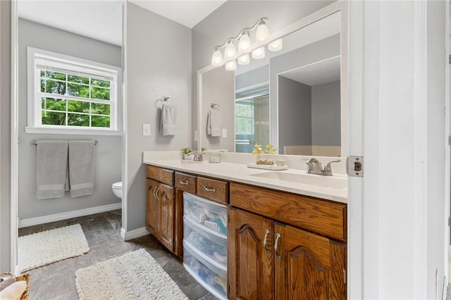 bathroom featuring double vanity, toilet, baseboards, and a sink