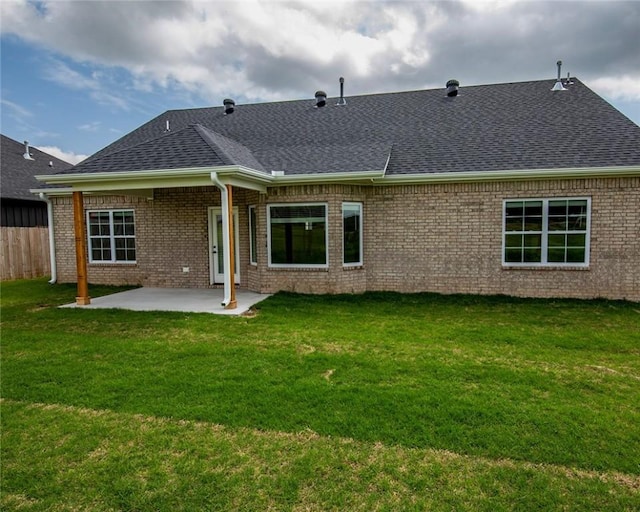 rear view of property with fence, a shingled roof, brick siding, a patio area, and a yard