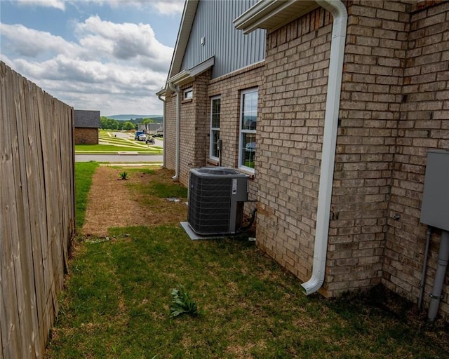 view of side of property featuring a yard, brick siding, and central AC