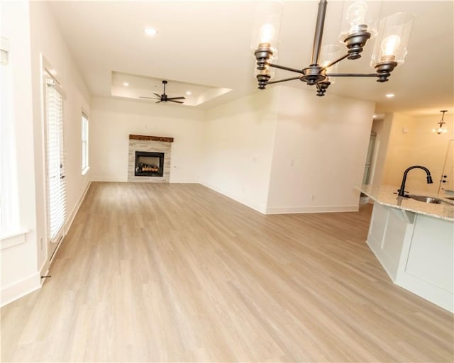 unfurnished living room with a sink, light wood-style flooring, ceiling fan with notable chandelier, baseboards, and a tile fireplace
