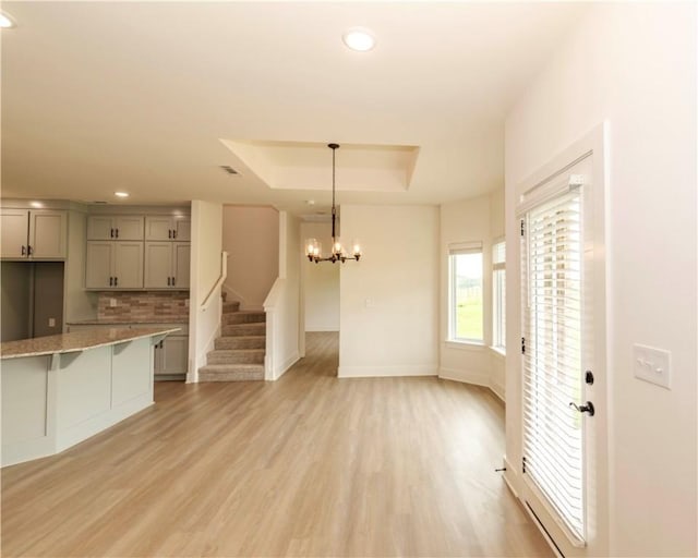 kitchen featuring light wood-style floors, a kitchen bar, gray cabinetry, a raised ceiling, and an inviting chandelier
