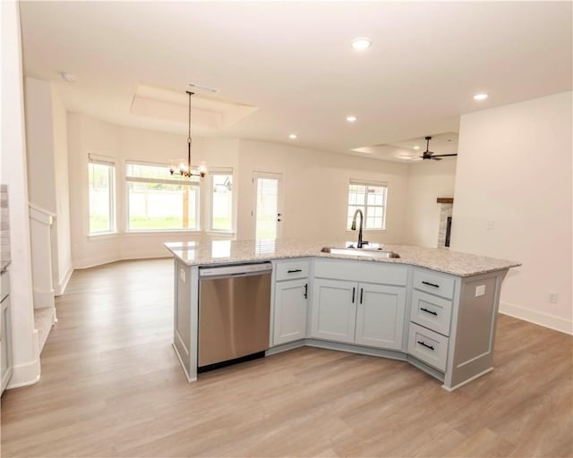 kitchen with stainless steel dishwasher, a sink, light wood-style floors, and a tray ceiling
