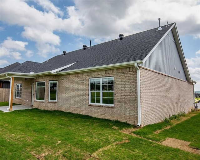 rear view of house featuring brick siding, roof with shingles, a yard, and a patio