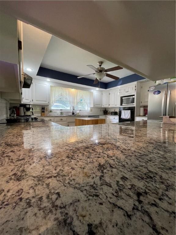 kitchen with white cabinetry, a tray ceiling, light stone countertops, and black appliances
