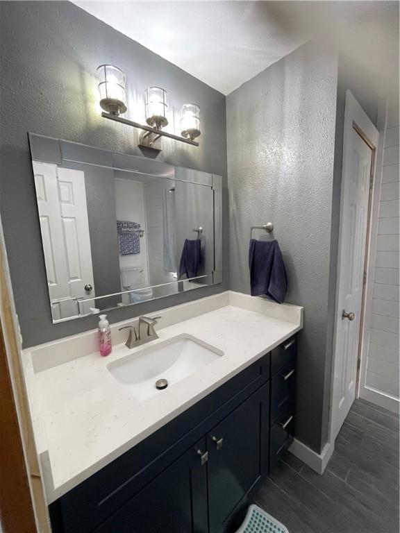 bathroom featuring vanity, a textured wall, baseboards, and wood finished floors