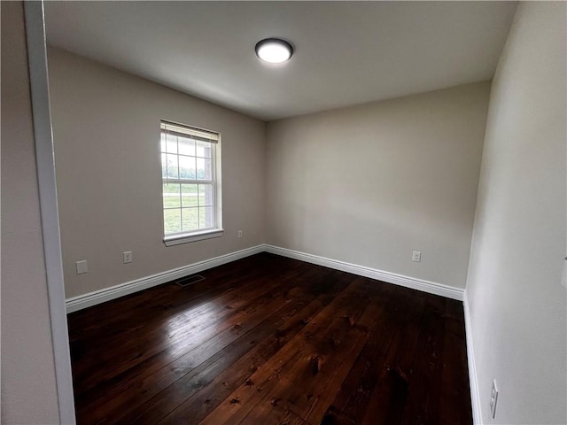 spare room featuring baseboards, dark wood-style flooring, and visible vents