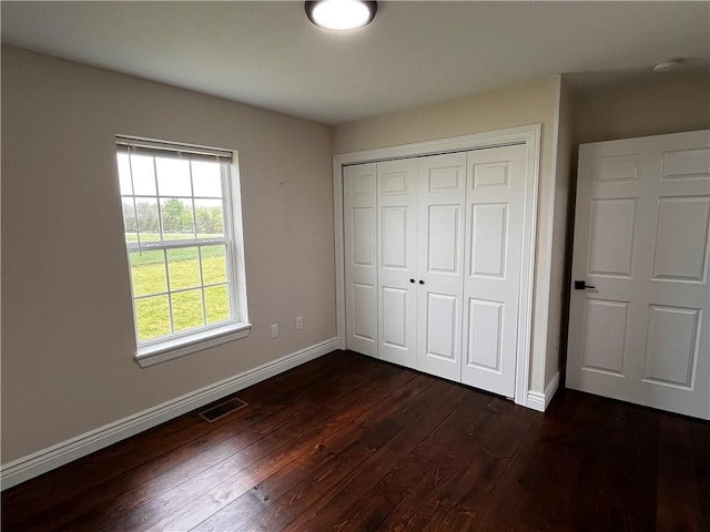 unfurnished bedroom featuring dark wood-style flooring, baseboards, visible vents, and a closet