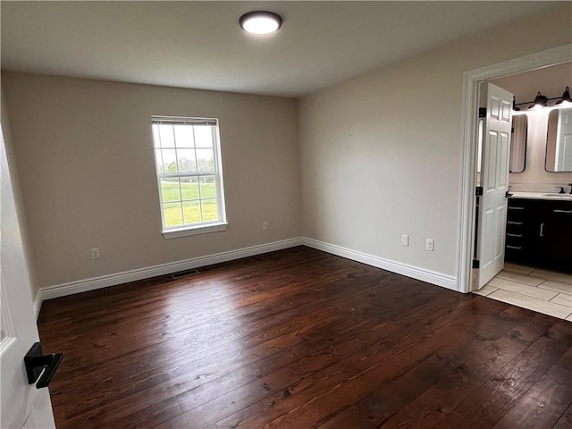 unfurnished bedroom featuring visible vents, hardwood / wood-style floors, baseboards, a sink, and ensuite bath