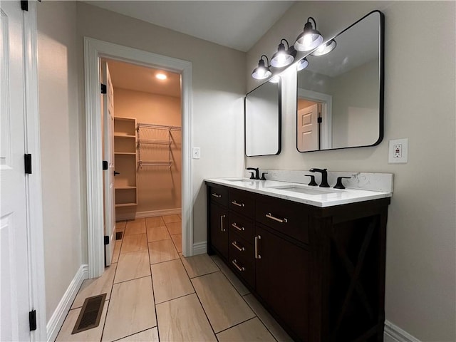 bathroom featuring double vanity, a walk in closet, visible vents, a sink, and baseboards