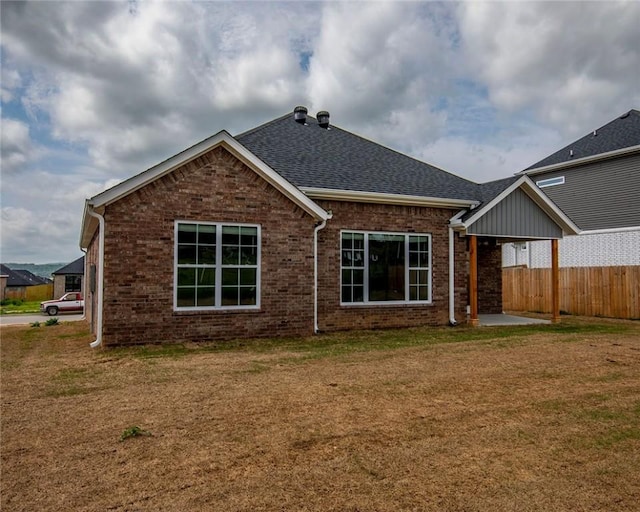 back of house with a yard, brick siding, fence, and a shingled roof