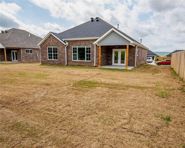 rear view of house with a lawn, brick siding, french doors, and a shingled roof