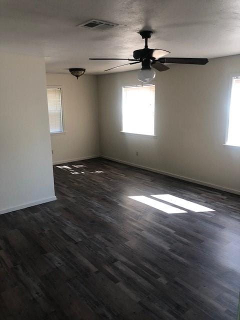 unfurnished room with a ceiling fan, baseboards, visible vents, and dark wood finished floors