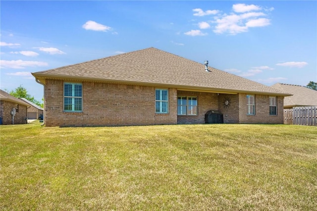 rear view of property with a lawn, a shingled roof, fence, and brick siding