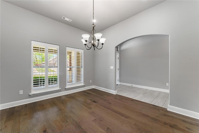 empty room with visible vents, arched walkways, wood finished floors, baseboards, and a chandelier