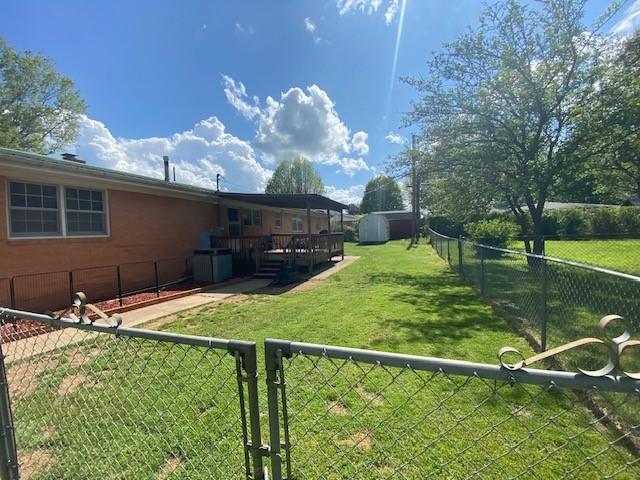 view of yard featuring an outdoor structure, a wooden deck, a fenced backyard, and a shed