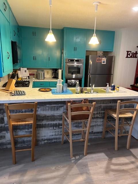 kitchen featuring pendant lighting, a peninsula, a kitchen bar, and stainless steel appliances