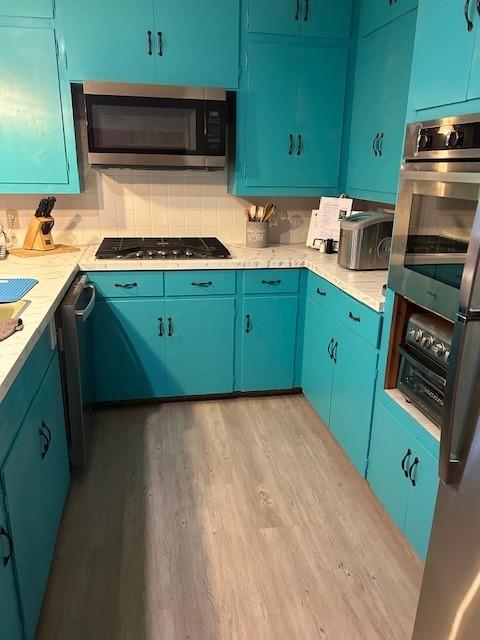 kitchen with light countertops, appliances with stainless steel finishes, wood finished floors, and tasteful backsplash