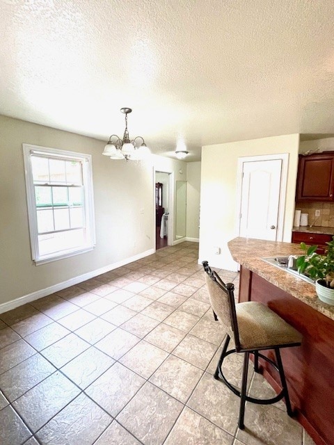 dining area with light tile patterned flooring, a textured ceiling, a notable chandelier, and baseboards