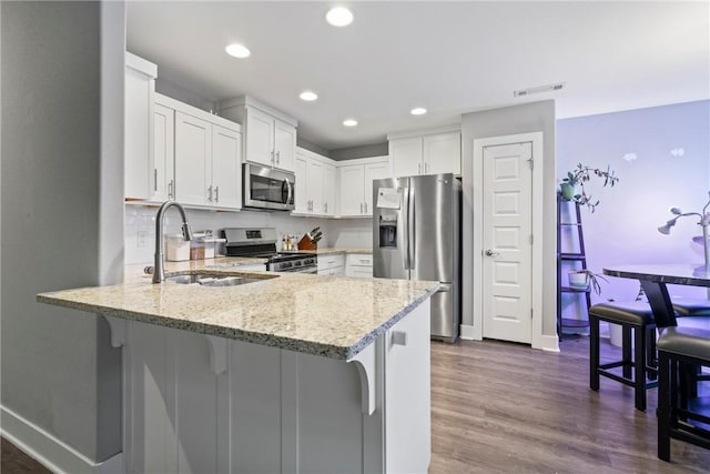 kitchen with light stone counters, a sink, stainless steel appliances, white cabinetry, and a peninsula