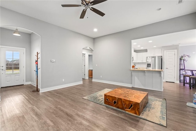 living area with baseboards, arched walkways, ceiling fan, and wood finished floors