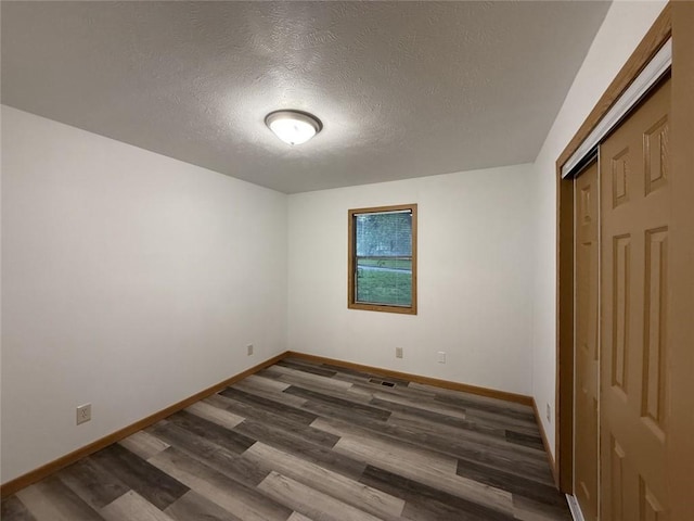 unfurnished bedroom with baseboards, dark wood-style floors, and a textured ceiling