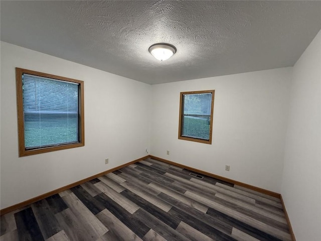 unfurnished room featuring baseboards, dark wood-style flooring, a textured ceiling, and a wealth of natural light