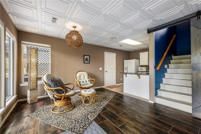 living area featuring a barn door, stairs, baseboards, dark wood-type flooring, and visible vents