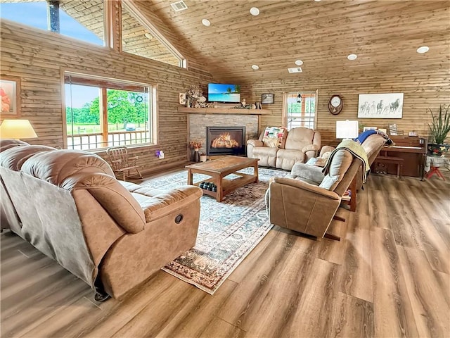 living room with wood walls, wood finished floors, a stone fireplace, high vaulted ceiling, and wooden ceiling