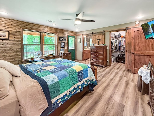 bedroom featuring a walk in closet, visible vents, wood walls, a barn door, and light wood-style flooring