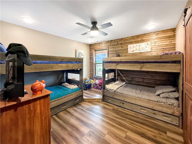bedroom featuring wooden walls, a ceiling fan, and wood finished floors